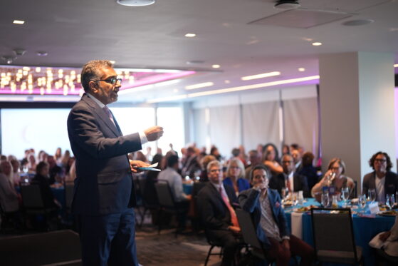 Dr. Ali Khan standing on a stage speaking to a room full of people at Raise Your Voice 2025